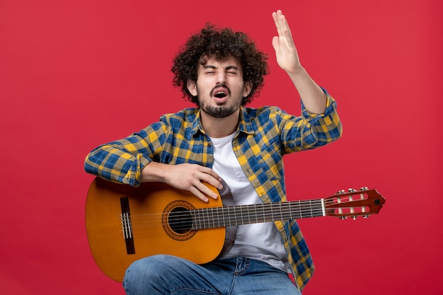 Vorderansicht junger Mann sitzt mit Gitarre auf roter Wand spielen Konzert Live-Farbmusiker Applaus Band