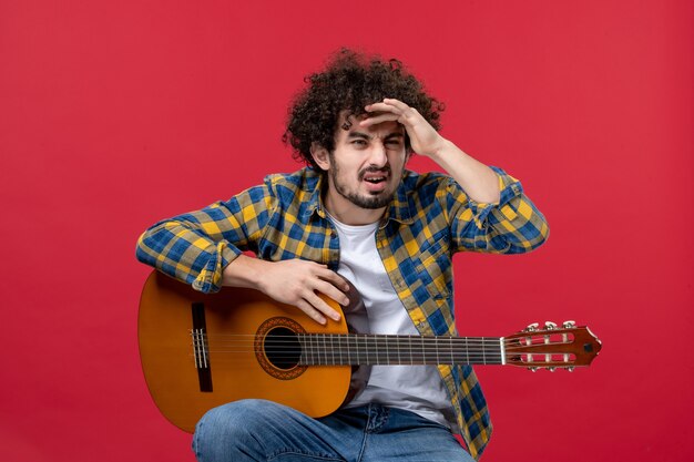 Vorderansicht junger Mann sitzt mit Gitarre auf roter Wand spielen Konzert Live-Musik Musiker Applaus Band