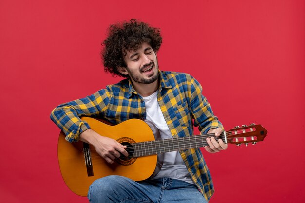 Vorderansicht junger Mann sitzt und spielt Gitarre auf der roten Wand Live-Konzert Farbmusiker Applaus Band Musik spielen