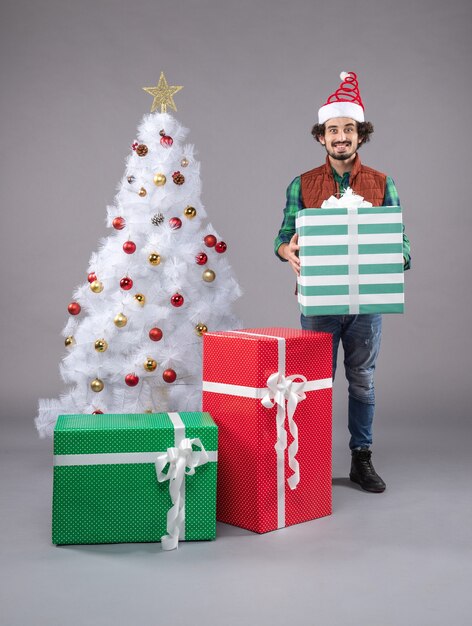 Vorderansicht junger Mann um Geschenke auf grauem Boden Weihnachtsgeschenk neues Jahr