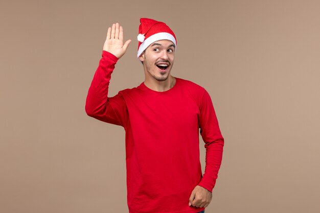 Vorderansicht junger Mann winkt und grüßt auf braunem Hintergrundweihnachtsgefühl-Feiertagsmann