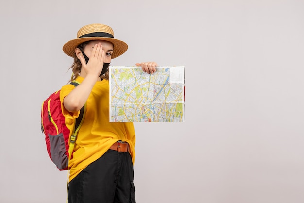 Vorderansicht junger Reisender mit Rucksack, der die Karte hochhält und die Hand auf ihr Auge legt