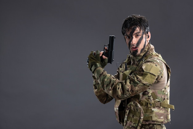 Kostenloses Foto vorderansicht junger soldat, der in tarnung mit gewehr an der dunklen wand kämpft