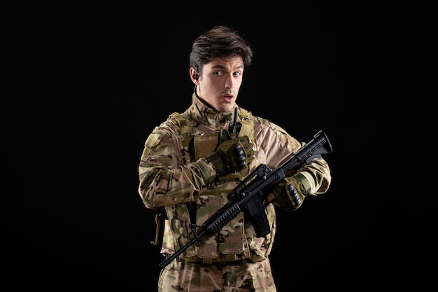 Vorderansicht junger Soldat in Uniform mit Gewehr auf schwarzer Wand