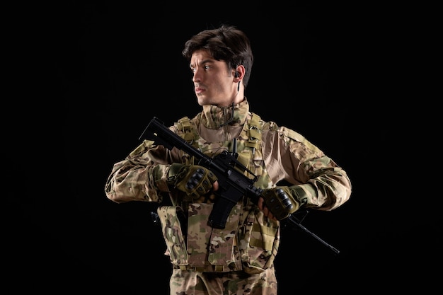 Vorderansicht junger Soldat in Uniform mit Gewehr auf schwarzer Wand