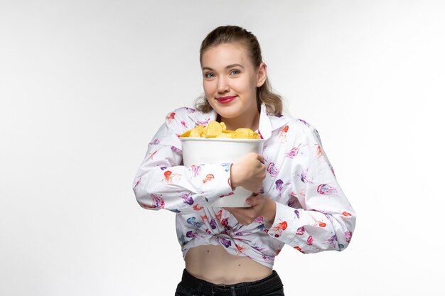Vorderansicht junger weiblicher Haltekorb mit Kartoffelchips, die auf einer weißen Oberfläche lächeln