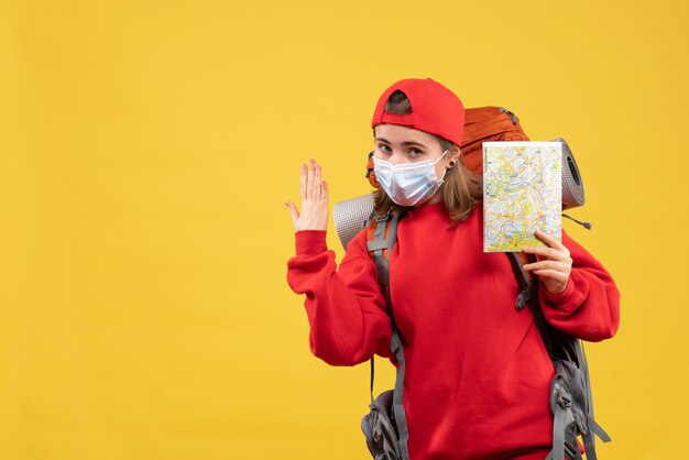 Vorderansicht junger weiblicher Reisender mit Rucksack und Maske, die Karte anhebende Hand hält