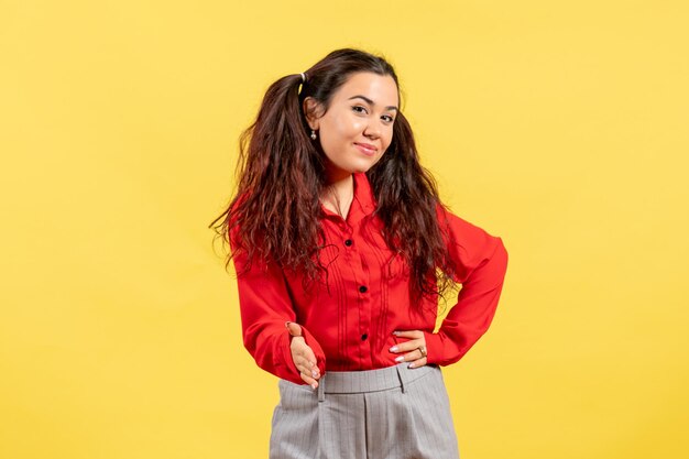 Vorderansicht junges Mädchen in roter Bluse mit süßem Haar, das versucht, Hände auf gelbem Hintergrund zu schütteln
