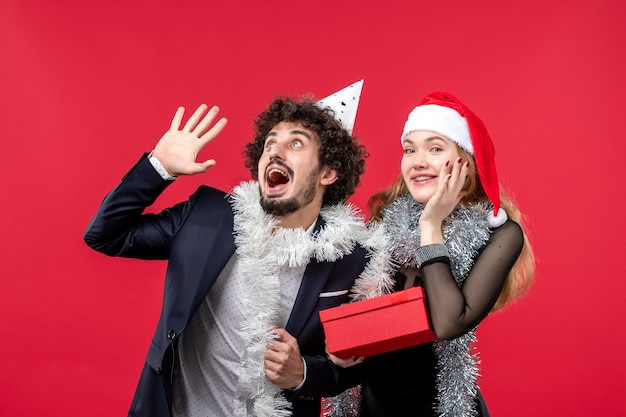 Vorderansicht junges Paar mit Neujahrsgeschenk auf roter Wandfarbe Weihnachtsliebesfeier