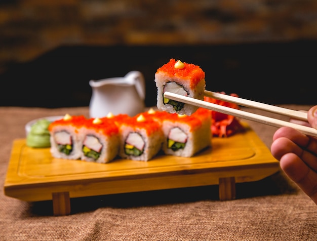 Vorderansicht Kalifornien Sushi-Rollen mit Wassabi und Ingwer auf einem Brett eine männliche Hand hält eine Rolle Essstäbchen