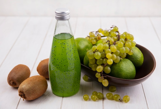 Vorderansicht Kiwi mit einer Flasche Saft ein Apfel und Trauben mit Mandarinen in einer Schüssel auf einer weißen Wand