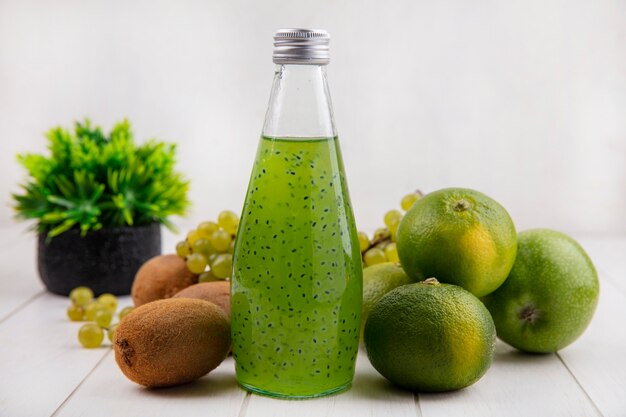 Vorderansicht Kiwi mit einer Flasche Saft Trauben und Mandarinen auf einer weißen Wand