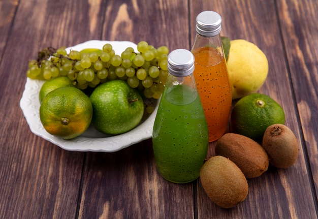 Vorderansicht Kiwi mit Mandarinen-Äpfeltrauben und Saft in Flaschen auf Holzwand