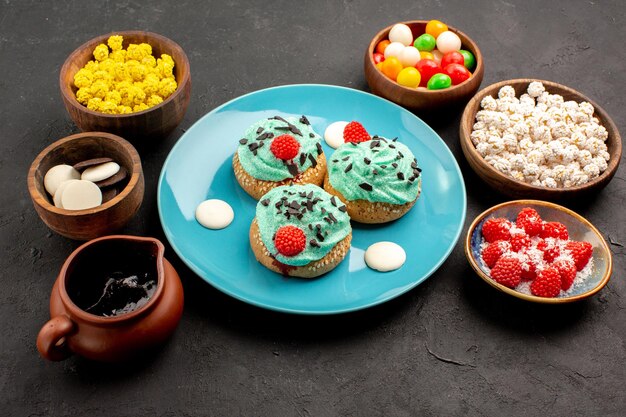 Vorderansicht kleine cremige Kuchen mit Süßigkeiten auf dunkelgrauem Hintergrund Dessertkuchen Keks Süßigkeiten Keksfarbe