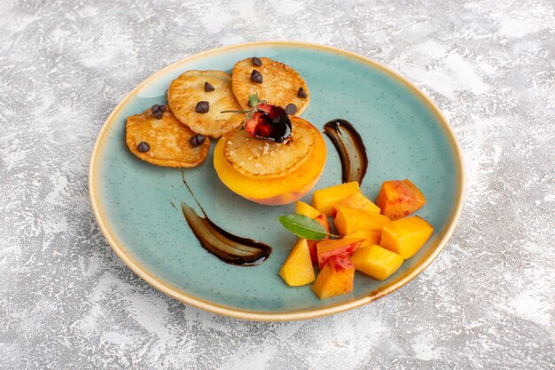 Vorderansicht kleine Keksgebäck innerhalb Platte mit frisch geschnittenen Pfirsichen auf hellem Tisch, Kuchenkekszucker süßes Gebäck Obst