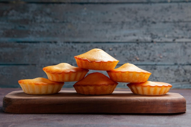 Vorderansicht kleine leckere Kuchen, die auf dem dunklen Hintergrund aufeinander gesäumt sind, süßer Kuchenkeks-Keks-Tee-Kuchen