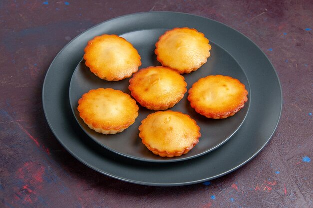 Vorderansicht kleine leckere Kuchen in der Platte auf dem dunklen Hintergrund Kuchen Keks Kuchen süßer Tee Keks Zucker