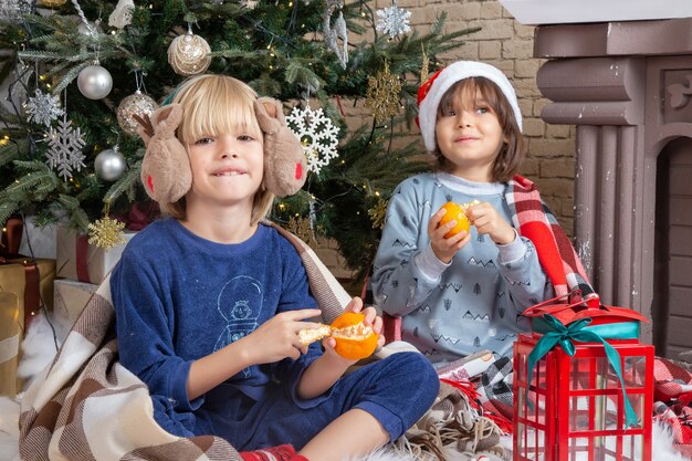 Vorderansicht kleine süße Jungs sitzen um den Weihnachtsbaum und präsentieren in ihrem Haus Mandarinenkind?