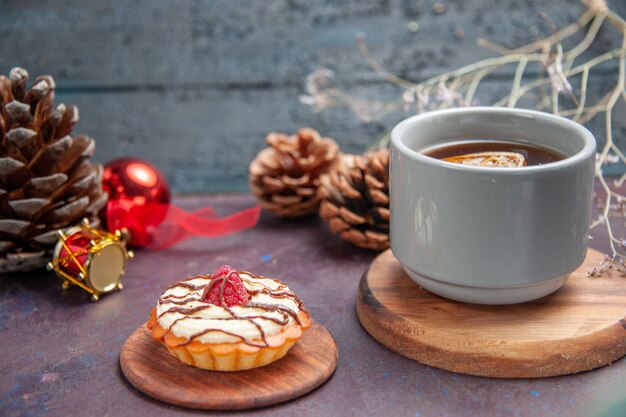 Vorderansicht kleiner cremiger Kuchen mit Tasse Tee auf dunklem Hintergrund Tortenkeks süßer Zuckerplätzchenkuchen