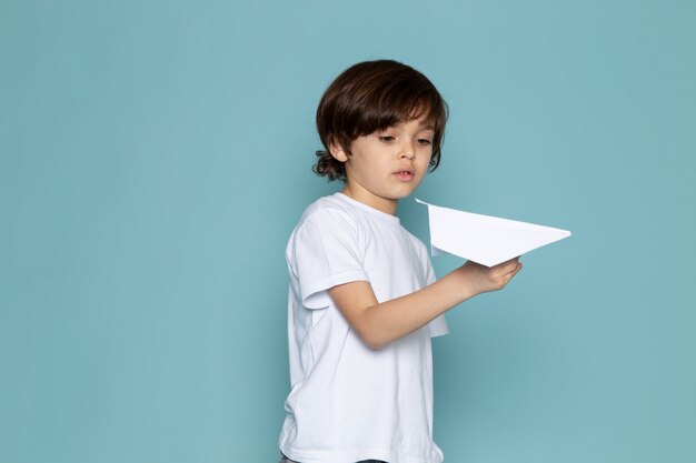 Vorderansicht kleiner Junge, der mit Papierflugzeug auf dem blauen Schreibtisch spielt