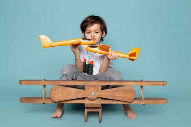 Vorderansicht kleiner Junge, der mit Spielzeugflugzeugen auf dem blauen Boden spielt