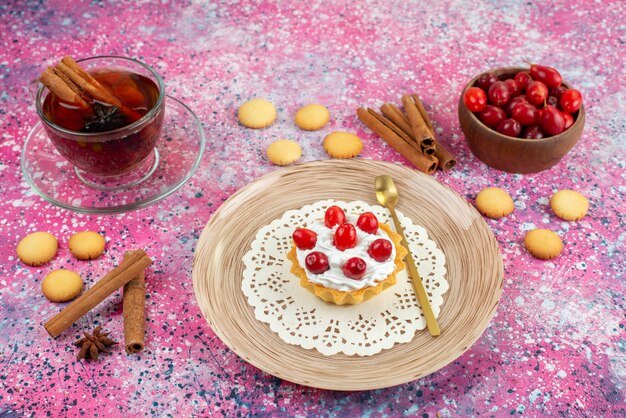 Vorderansicht kleiner Kuchen mit frischer Sahne und frischen Früchten zusammen mit Zimt und Tasse Tee auf dem hellen Schreibtischkuchen süß