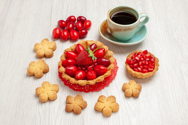 Vorderansicht kleiner Kuchen mit Früchten und Tasse Tee auf weißem Schreibtischfruchtdessertkuchen