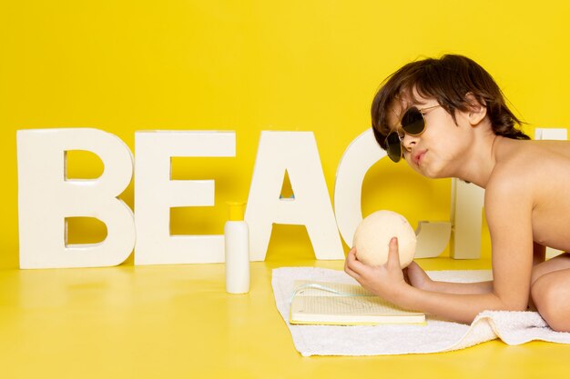 Vorderansicht kleiner süßer Junge in der Sonnenbrille nahe Strandwort auf gelb