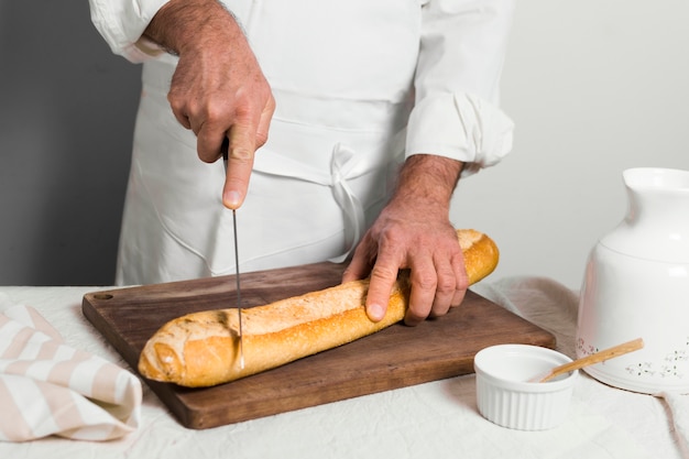 Vorderansicht-Koch, der weiße Kleidung trägt, die ein Baguette schneidet