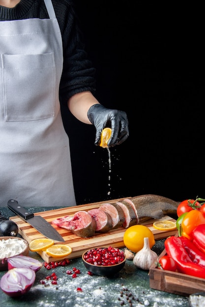 Vorderansicht Koch drückt Zitrone auf rohen Fischscheiben Messer auf Schneidebrett auf Küchentisch