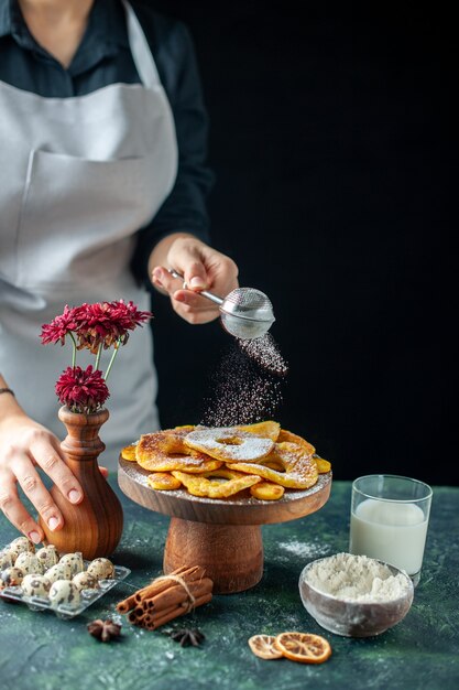 Vorderansicht Köchin gießt Zuckerpulver auf getrocknete Ananasringe auf dem dunklen Obstkochjob Arbeiter Gebäck Kuchen Kuchenbäckerei