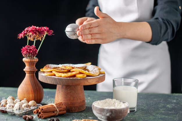 Vorderansicht Köchin gießt Zuckerpulver auf getrocknete Ananasringe auf einem dunklen Obst Job Gebäck Kuchen Kuchen Bäckerei Kochen