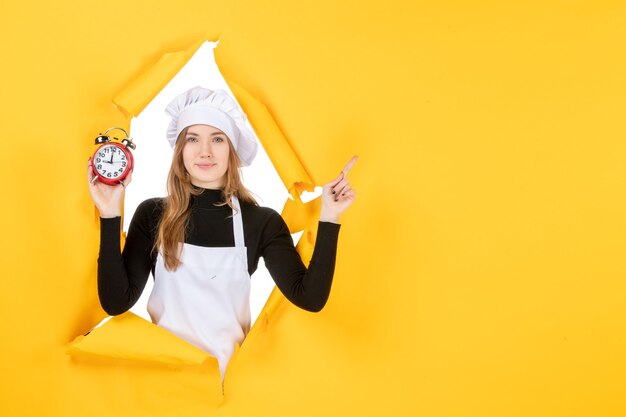 Vorderansicht Köchin hält Uhren auf gelbem Essen Foto Farbe Job Küche Küche Emotion Zeit