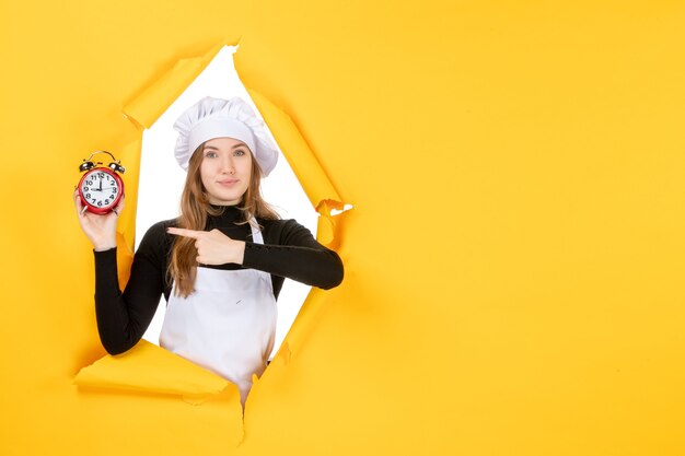 Vorderansicht Köchin hält Uhren auf gelber Zeit Essen Foto Job Küche Emotionen Sonne Küche Farbe