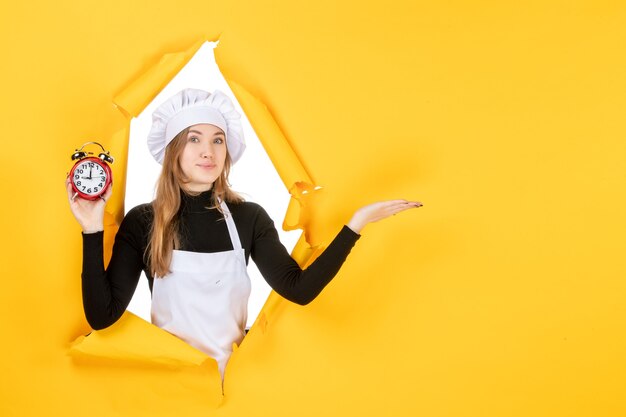 Kostenloses Foto vorderansicht köchin hält uhren auf gelber zeit lebensmittelfarbe job küche emotion sonne küche