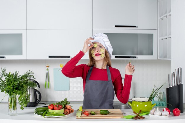 Vorderansicht Köchin in Kochmütze, die Gurkenscheiben auf ihr Gesicht legt