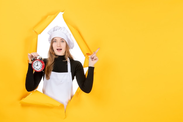 Kostenloses Foto vorderansicht köchin in weißer kochmütze mit uhr auf gelbem foto farbjob emotion küche küche sonne essen