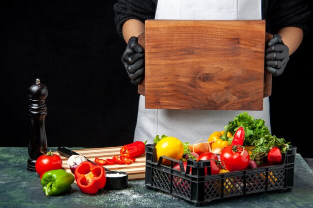 Vorderansicht Köchin mit Holzschreibtisch mit frischem Gemüse auf dem Tisch auf dunkler Lebensmittelfarbe Salatküche Küche Mahlzeit