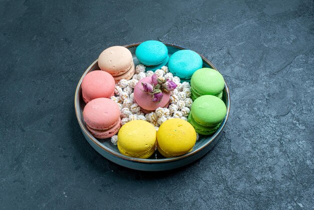 Vorderansicht köstliche französische macarons mit bonbons im tablett auf dunklem raum