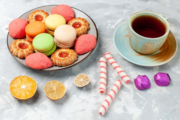 Vorderansicht köstliche französische Macarons mit Keksen Bonbons und Tee auf hellweißer Oberfläche backen Kuchen Keks Zucker süß