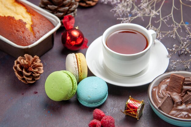 Vorderansicht köstliche französische macarons mit schokolade und tasse tee auf dunklem hintergrund