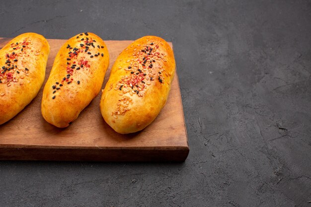 Vorderansicht köstliche gebackene Pastetchen frisch aus dem Ofen auf dunkelgrauem Hintergrundkuchengebäck-Teigofen-Fleischkuchen backen