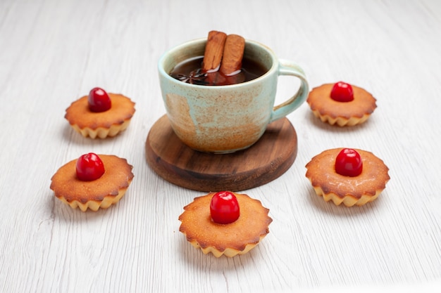 Vorderansicht köstliche kleine Kuchen mit Tasse Tee auf weißem Schreibtischkuchen-Dessert süßer Keks