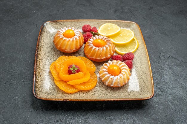 Vorderansicht köstliche kleine Kuchen mit Zitronenscheiben und Mandarinen auf dunklem Raum