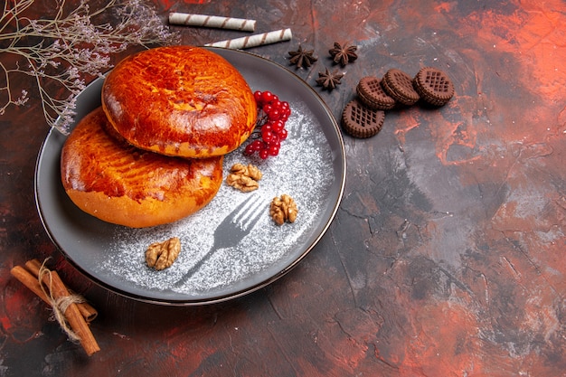 Vorderansicht köstliche Kuchen mit roten Beeren auf dunklem Gebäckkuchen des dunklen Tischkuchens