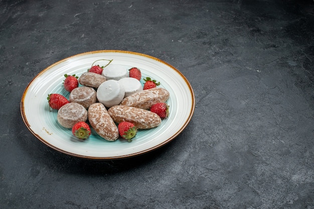 Vorderansicht köstliche Lebkuchen mit frischen roten Erdbeeren auf dunkelgrauem Schreibtischkuchenkekszucker-süßem Kuchen-Backkeks