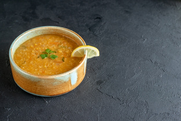 Vorderansicht köstliche Linsensuppe mit Zitronenscheibe innerhalb des kleinen Tellers auf dunkler Oberfläche