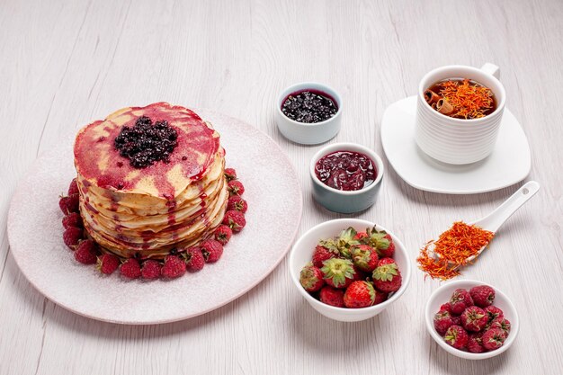 Vorderansicht köstliche Pfannkuchen mit Erdbeertasse Tee auf weißem Schreibtisch Kuchen Keks süße Fruchtkuchen Beere