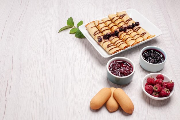 Vorderansicht köstliche Pfannkuchenröllchen mit Marmelade und Keksen auf weißem Raum