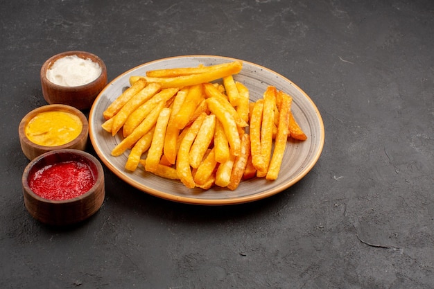 Vorderansicht köstliche Pommes frites mit Gewürzen auf dunklem Raum